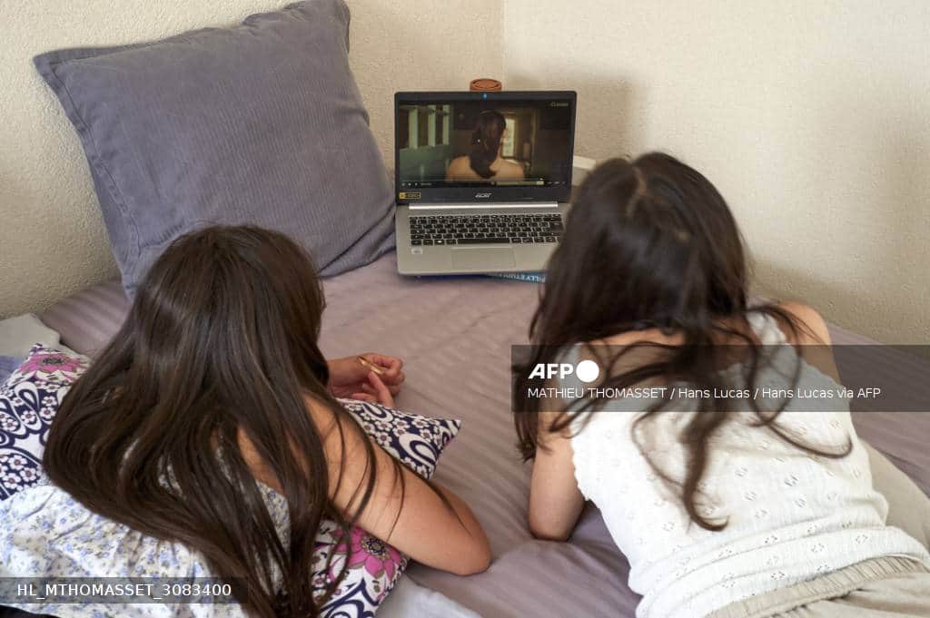 Deux enfants, vus de dos, regardent un ordinateur portable posé sur un lit