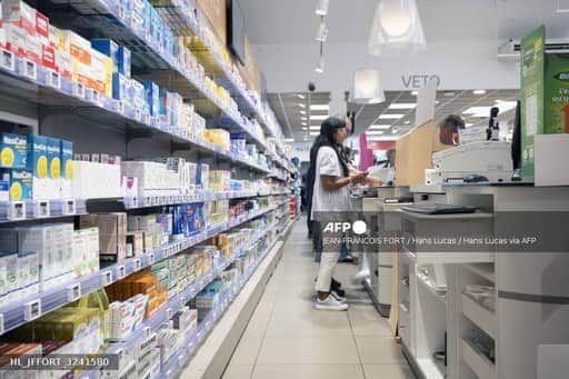 Une cliente devant les rayonnages de boîtes de médicaments d'une pharmacie française