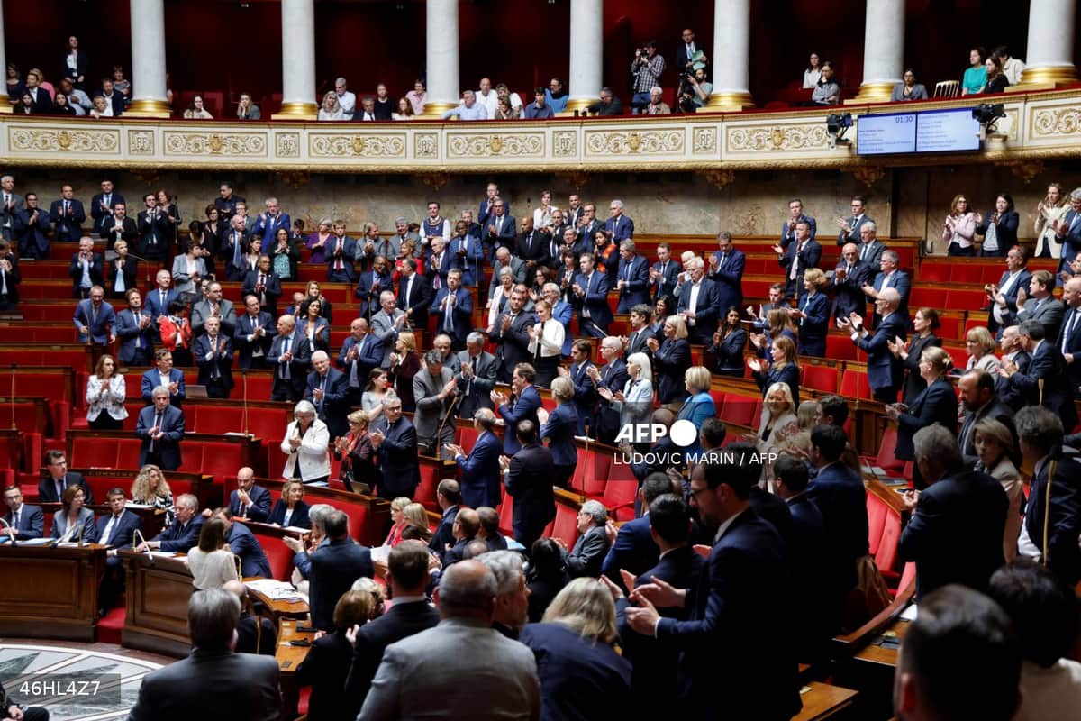 Vue de l'hémicycle de l'Assemblée nationale, à Paris, des députés debout en train d'applaudir.