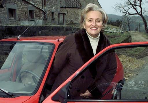 Bernadette Chirac, souriante, devant une voiture rouge dans un paysage de Corrèze