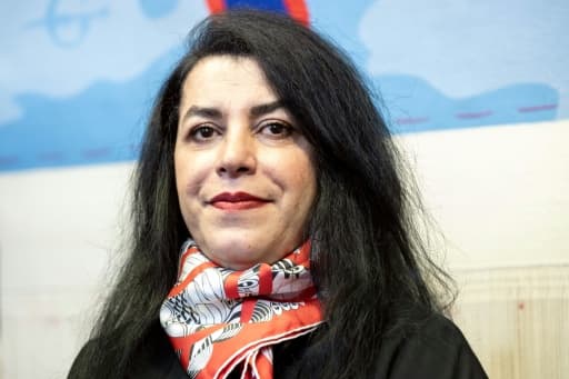 Portrait de Marjane Satrapi, un foulard rouge et blanc autour du cou, devant une de ses œuvres