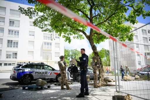 Un policier et deux militaires en faction derrière un ruban de sécurité, au pied d'immeubles