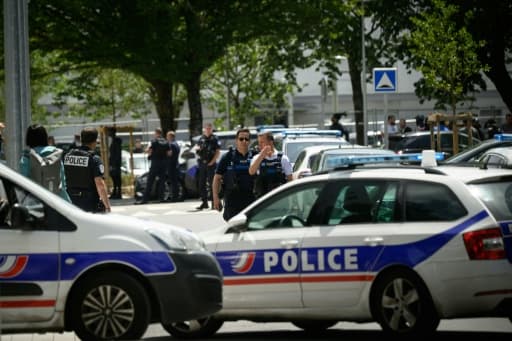 Des voitures de police et des policiers déployés sous les arbres, au pied d'immeubles