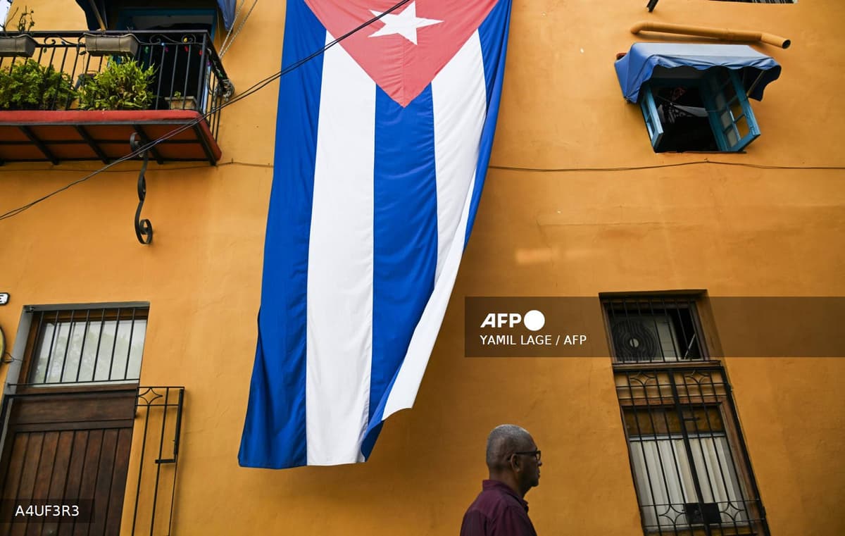 Un grand drapeau cubain déployé sur la façade d'un immeuble de La Havane, un passant marchant en dessous