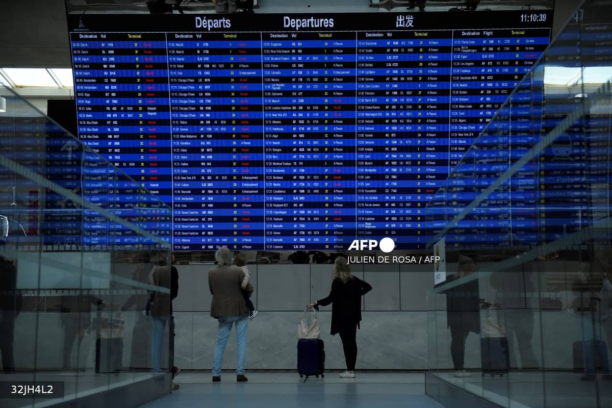 Des voyageurs devant le tableau des départs dans un aéroport français