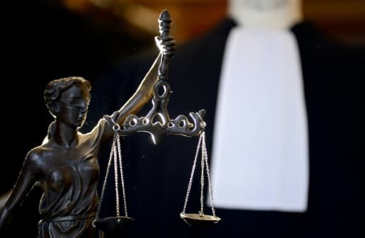 Une statue de la justice tenant une balance, devant la robe noire et le rabat blanc d'un avocat