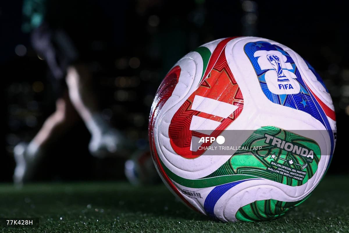 Le ballon officiel Trionda de la Coupe du monde 2026 posé sur la pelouse, un joueur en arrière-plan