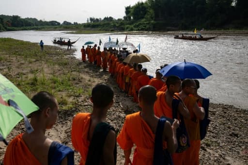 Des moines bouddhistes en robe safran marchent le long de la rivière Kok