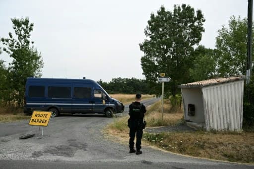 Un gendarme devant un fourgon et un panneau route barrée, sur la route du site des recherches dans le Tarn
