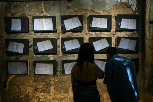 Des visiteurs devant des documents d’archives exposés sur un mur criblé d’impacts à Beit Beirut