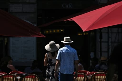 Un couple marche en plein soleil devant la terrasse d'un café