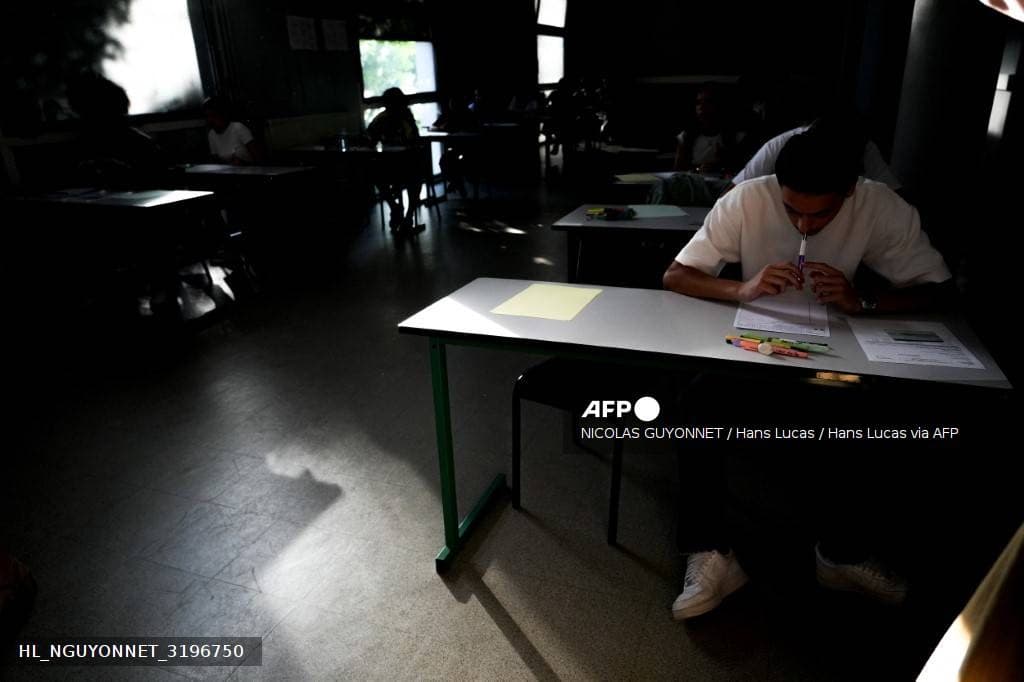 Des candidats du baccalauréat composent dans une salle plongée dans la pénombre, volets fermés
