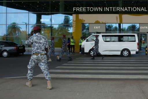 Des agents de sécurité escortent des migrants à leur arrivée à l'aéroport international de Freetown, en Sierra Leone