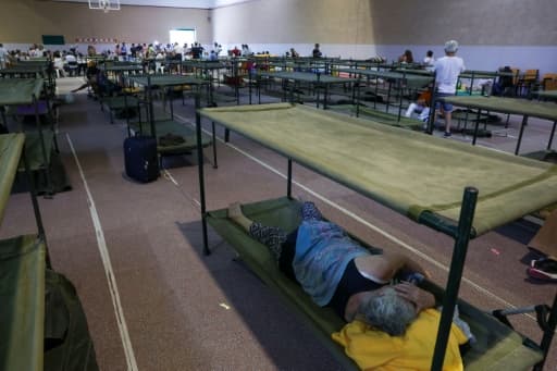 Une femme allongée sur un lit de camp dans un gymnase transformé en centre d'hébergement