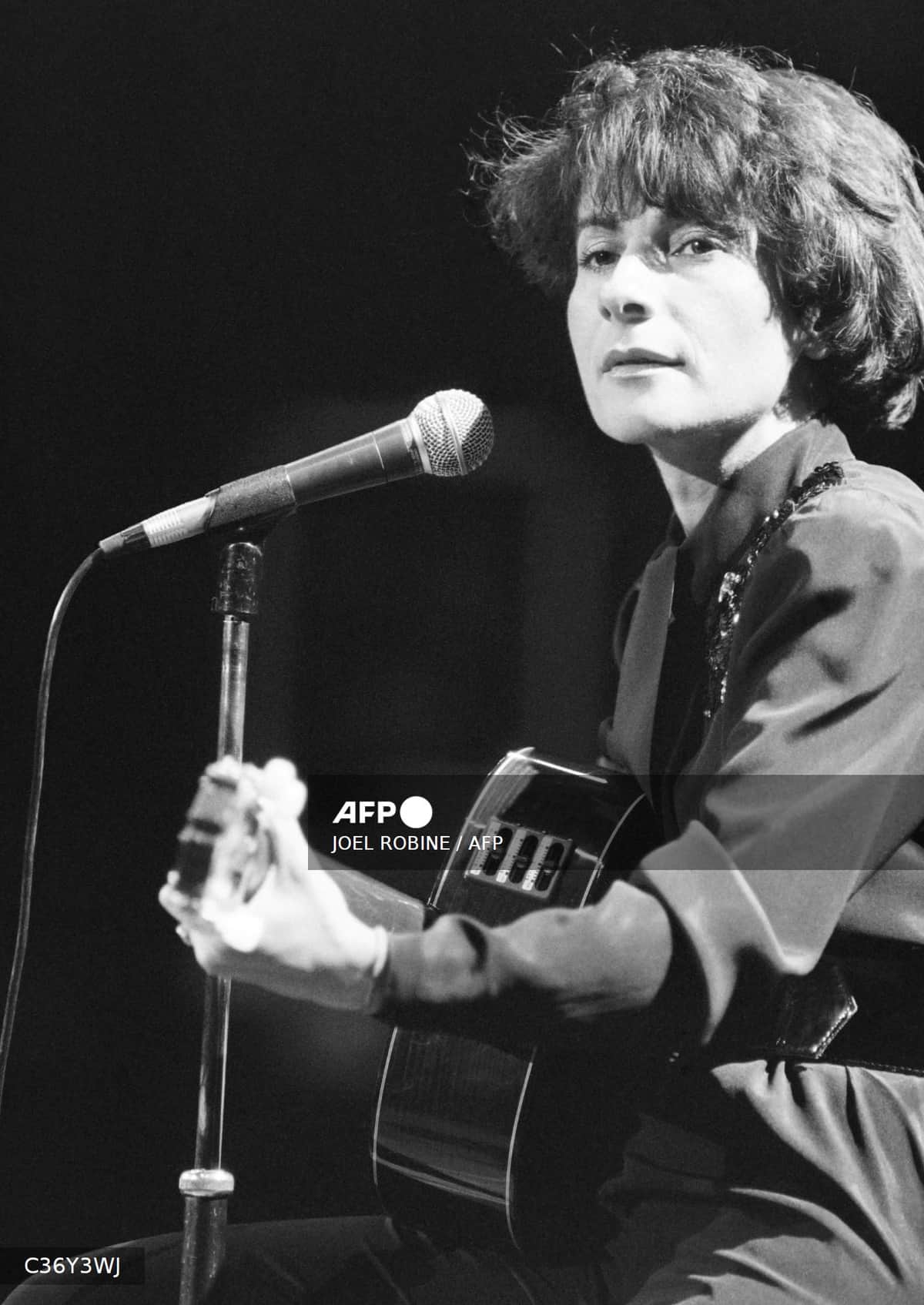 Marie-Paule Belle sur scène, guitare à la main, devant un micro