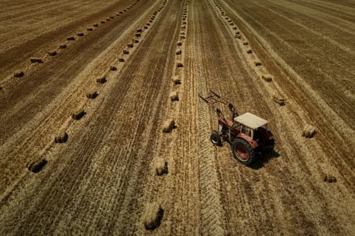 Vue aérienne d'un tracteur dans un champ moissonné parsemé de bottes de paille dans le Lot-et-Garonne