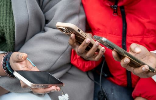 Des lycéens debout devant leur établissement, les yeux baissés sur leurs téléphones.