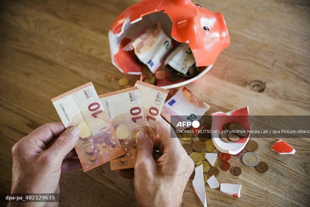 Des mains âgées comptent des billets de dix euros à côté d'une tirelire brisée d'où s'échappe de la monnaie