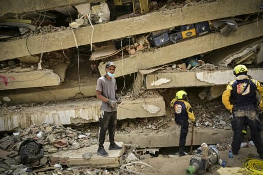 Homme debout sur les dalles effondrées d'un immeuble au Venezuela, secouristes à ses côtés