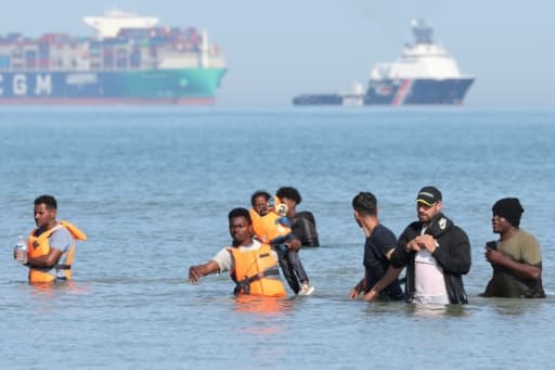 Des personnes en gilet de sauvetage avancent dans l'eau vers une embarcation, au large d'une plage du nord de la France