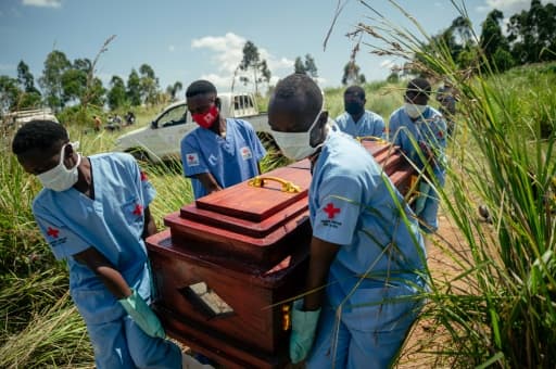 Des secouristes en tenue de protection portent un cercueil dans un cimetière