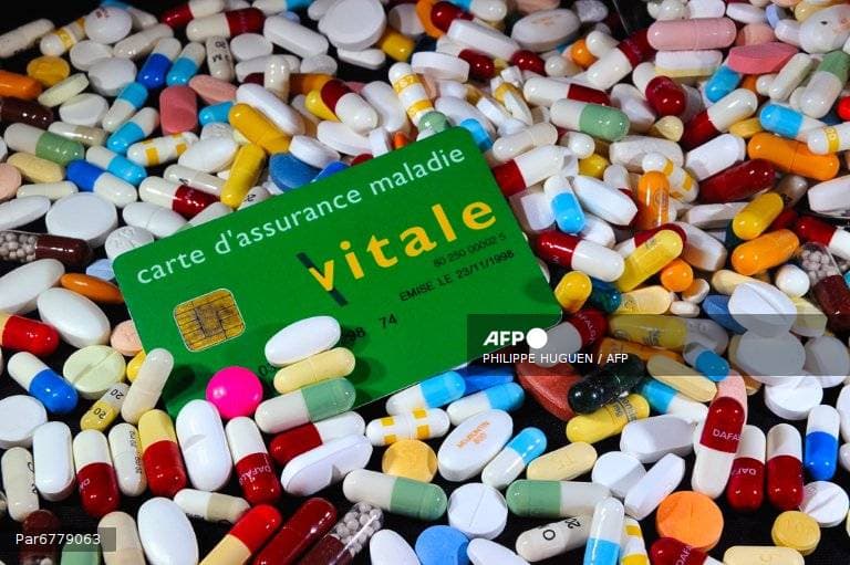 Une carte Vitale posée sur un lit de comprimés et de gélules de médicaments