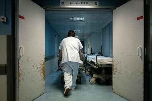 Un soignant vu de dos pousse un brancard vide dans le couloir d'un service d'urgences