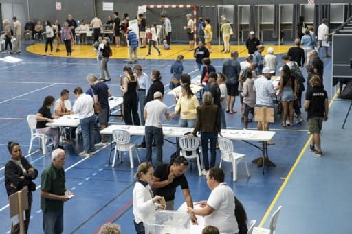 Des électeurs autour de tables de vote installées dans un gymnase, à Nouméa