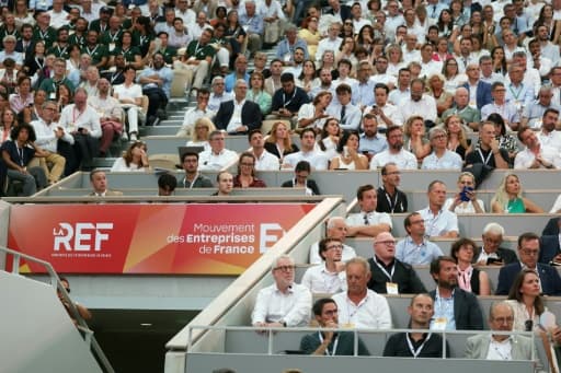 Des participants assis dans les tribunes d'un court de tennis devant une banderole de la REF du Medef