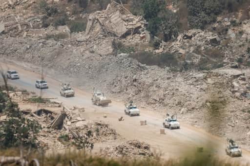 Une colonne de véhicules blindés blancs de l'ONU roule sur une route bordée de bâtiments effondrés