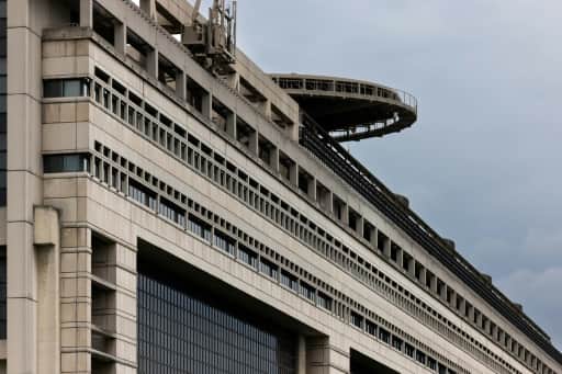 La façade de béton d'un grand bâtiment administratif, surmontée d'une plateforme ronde, sous un ciel gris