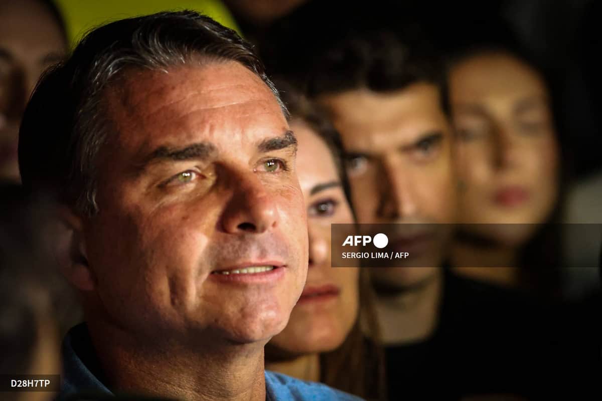 Flávio Bolsonaro en gros plan, le regard levé, devant trois personnes floues au second plan