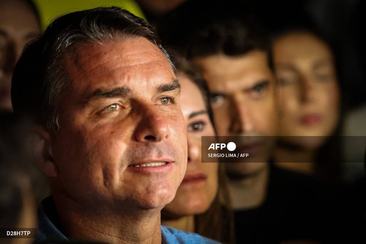 Flávio Bolsonaro en gros plan, le regard levé, devant trois personnes floues au second plan