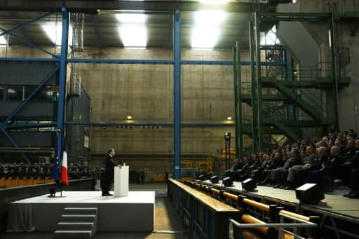 Emmanuel Macron au pupitre, dans un vaste hall industriel, devant des rangées de personnes assises