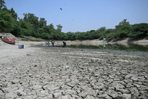 Vase craquelée au premier plan d'un lac en partie asséché, quelques personnes dans l'eau au fond