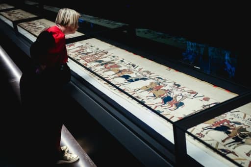 Une visiteuse penchée au-dessus de la tapisserie de Bayeux posée à plat sous verre