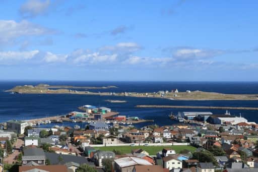 Vue en surplomb des maisons colorées de Saint-Pierre, du port et d'une île basse au large, sous un ciel bleu