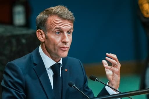 Emmanuel Macron parle derrière des micros, la main droite levée