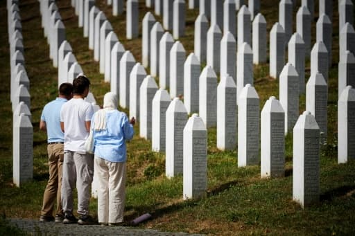 Trois personnes de dos devant les stèles blanches d'un cimetière mémorial