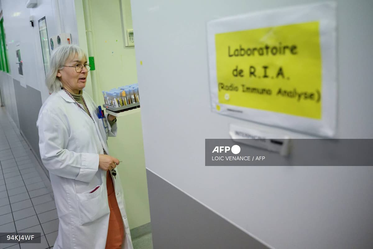 Une soignante en blouse blanche dans un couloir d'hôpital devant un laboratoire d'analyses