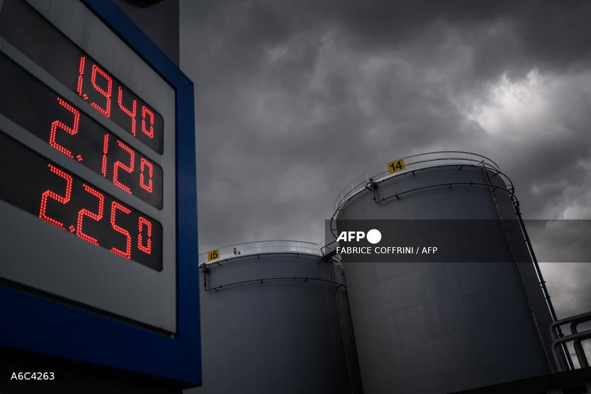 Affichage LED des prix de carburant en rouge devant des cuves de stockage sous un ciel menaçant