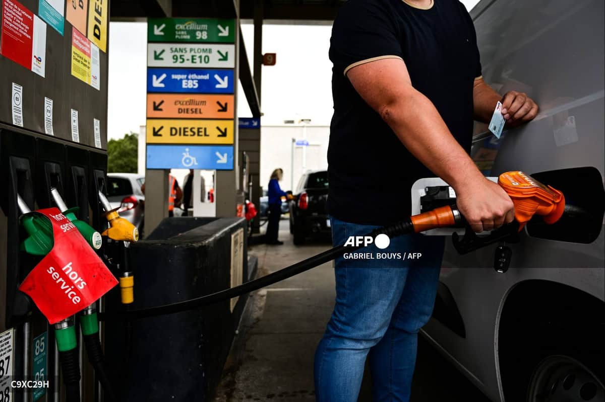 Un automobiliste fait le plein d'un véhicule à une pompe, devant les panneaux des carburants