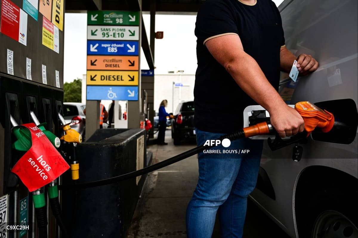 Un automobiliste fait le plein d'un véhicule à une pompe, devant les panneaux des carburants