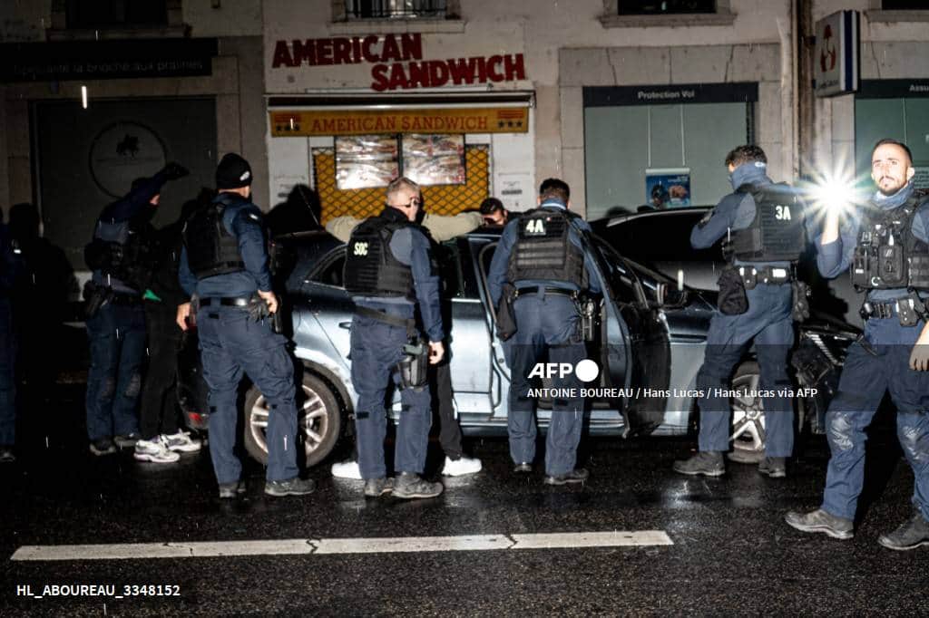 Des policiers de nuit autour d'une voiture arrêtée dans une rue de Lyon, deux passagers les mains sur le toit du véhicule