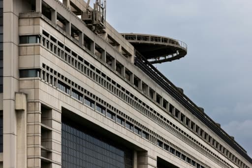 La façade de béton d'un grand bâtiment administratif, surmontée d'une plateforme ronde, sous un ciel gris