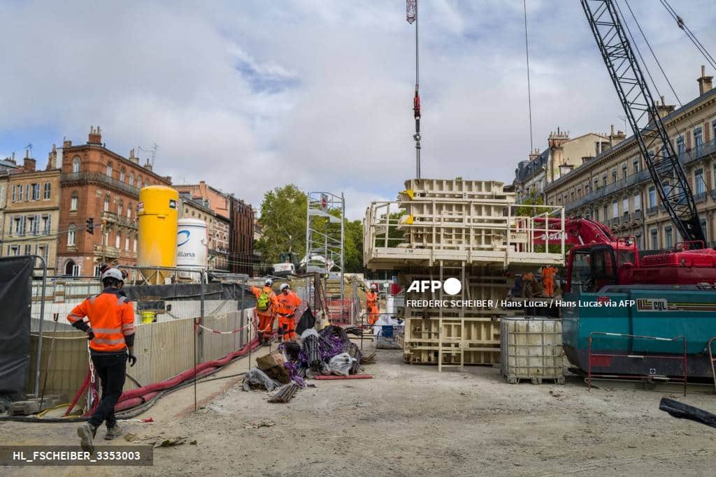 Des ouvriers en tenue orange sur un chantier de construction, entre une grue et des coffrages
