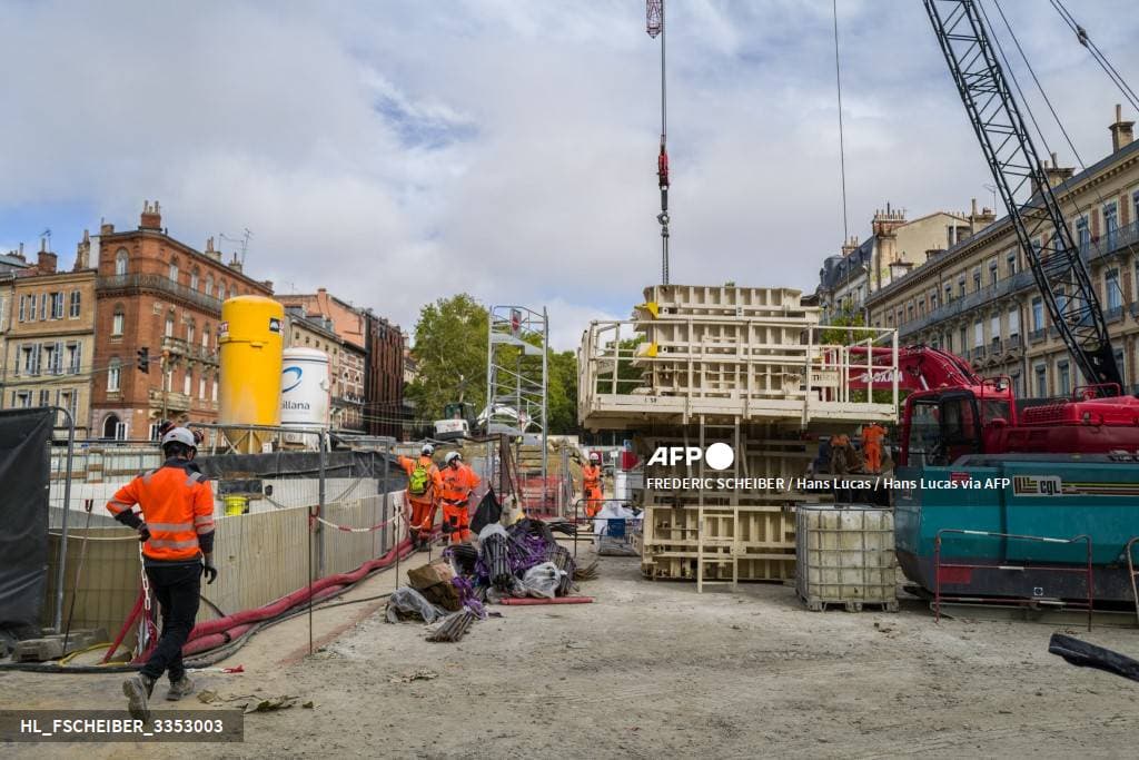 Des ouvriers en tenue orange sur un chantier de construction, entre une grue et des coffrages