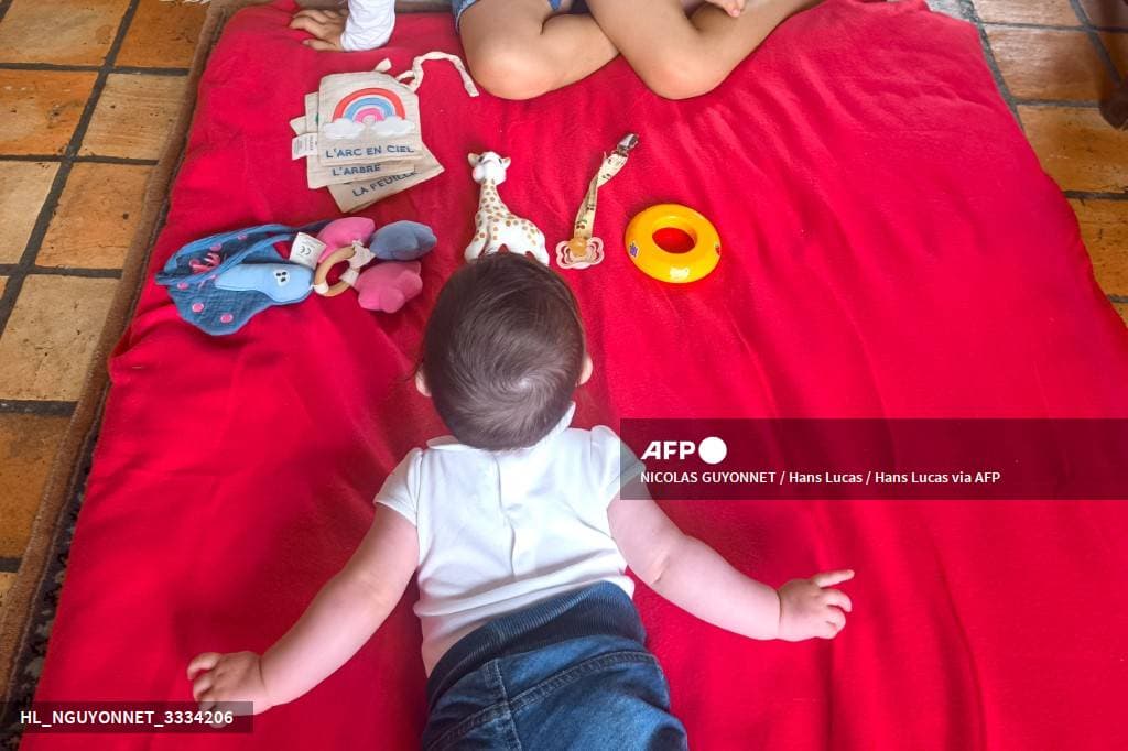 Un bébé vu de dos, à plat ventre sur une couverture rouge, face à des jouets d'éveil