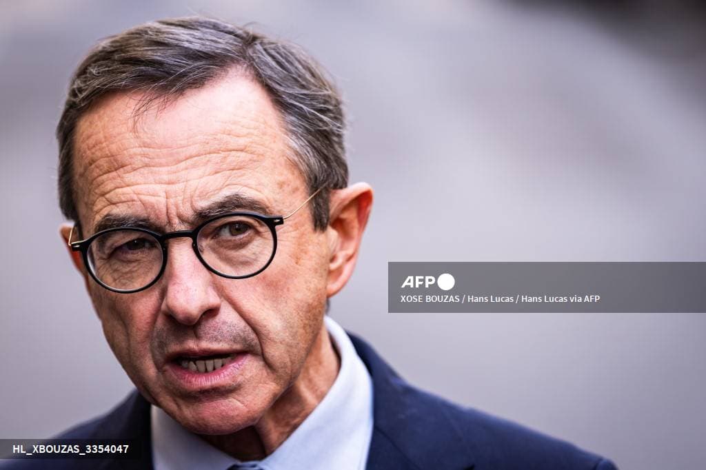 Portrait de Bruno Retailleau, en costume sombre et lunettes, parlant face à la presse