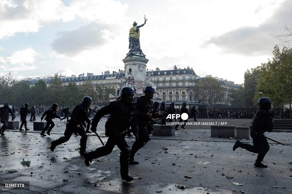 Des policiers casqués courent sur la place de la République, la statue de la République en arrière-plan